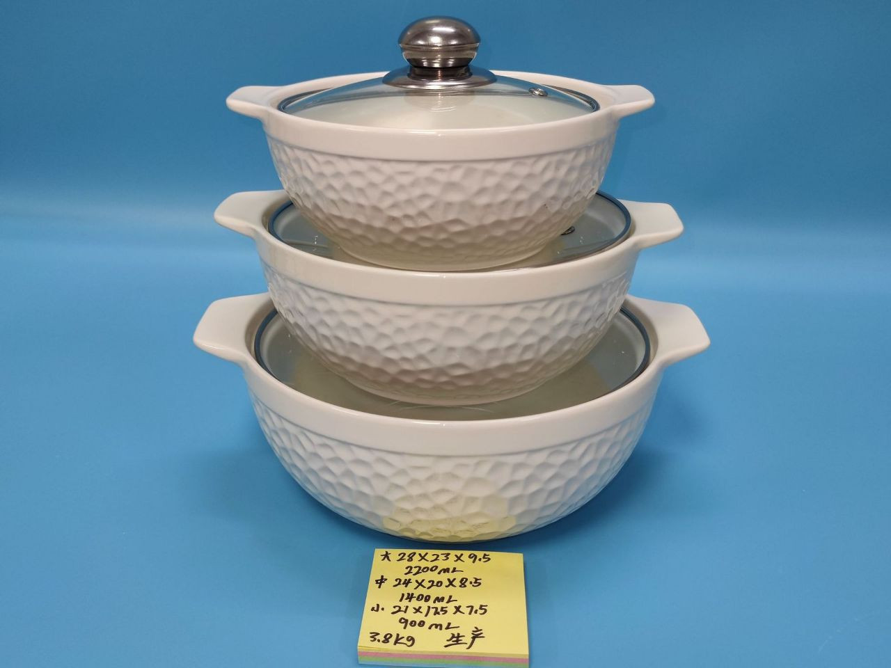 Un ensemble de trois bols de service ou cocottes en céramique empilables, de couleur blanche et de tailles différentes, chacun avec un couvercle en verre et une poignée métallique sur le dessus du cou